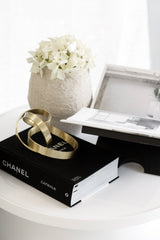 Gold infinity loop sculpture styled on black book beside textured vase and tray