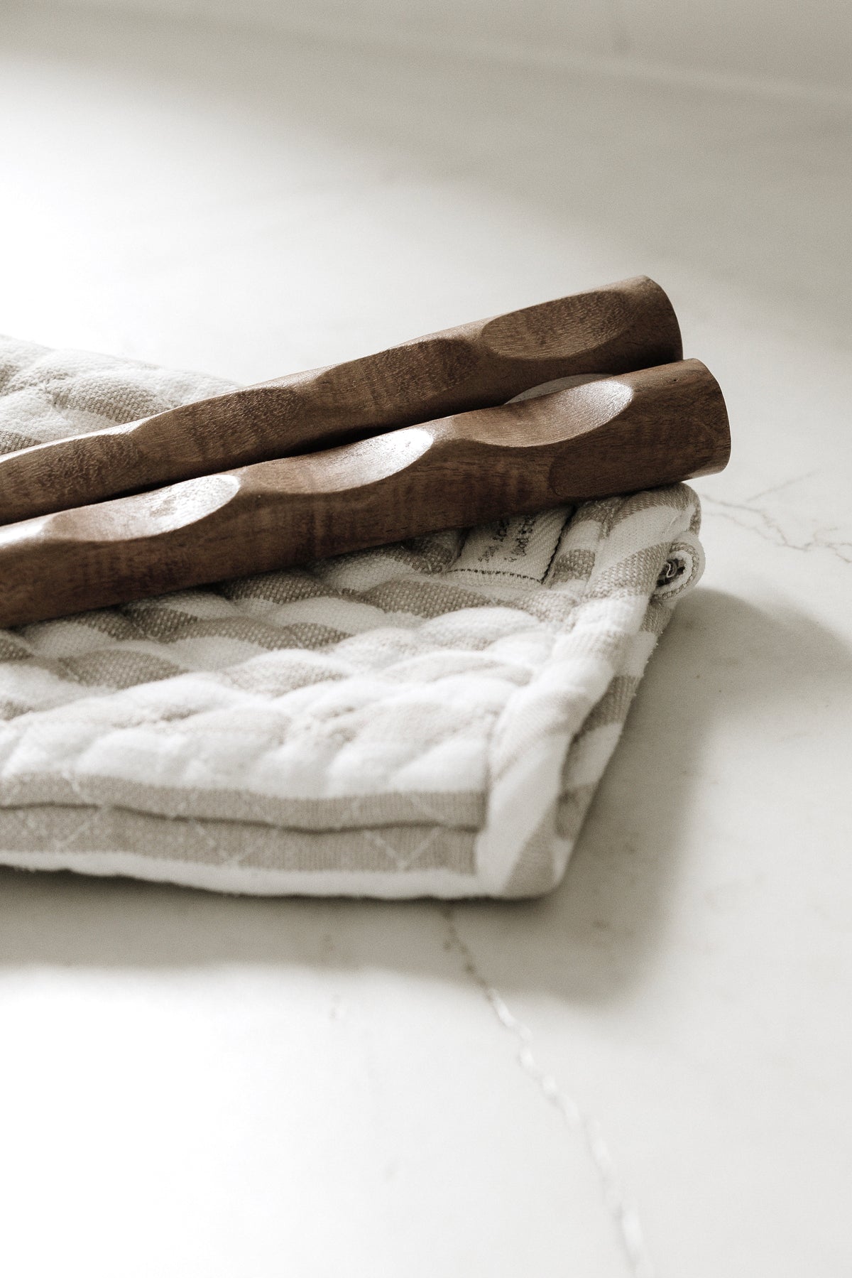 Twisted wooden handles of the gold and wood salad servers on a folded quilted cloth