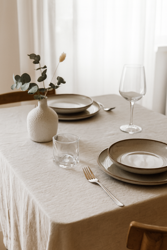 Clear glass tumbler on a linen-covered dining table with stoneware plates, a wine glass and a white bud vase