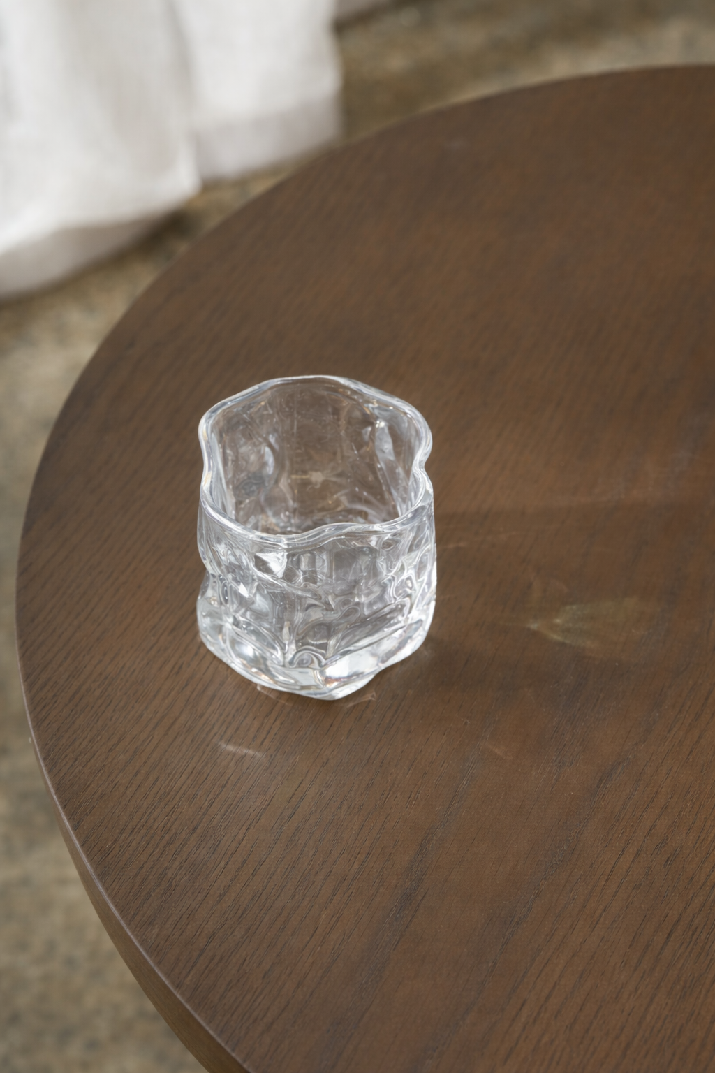 Gordon Tumbler by Ned Collections, a rippled mouth-blown clear glass tumbler on a dark timber table