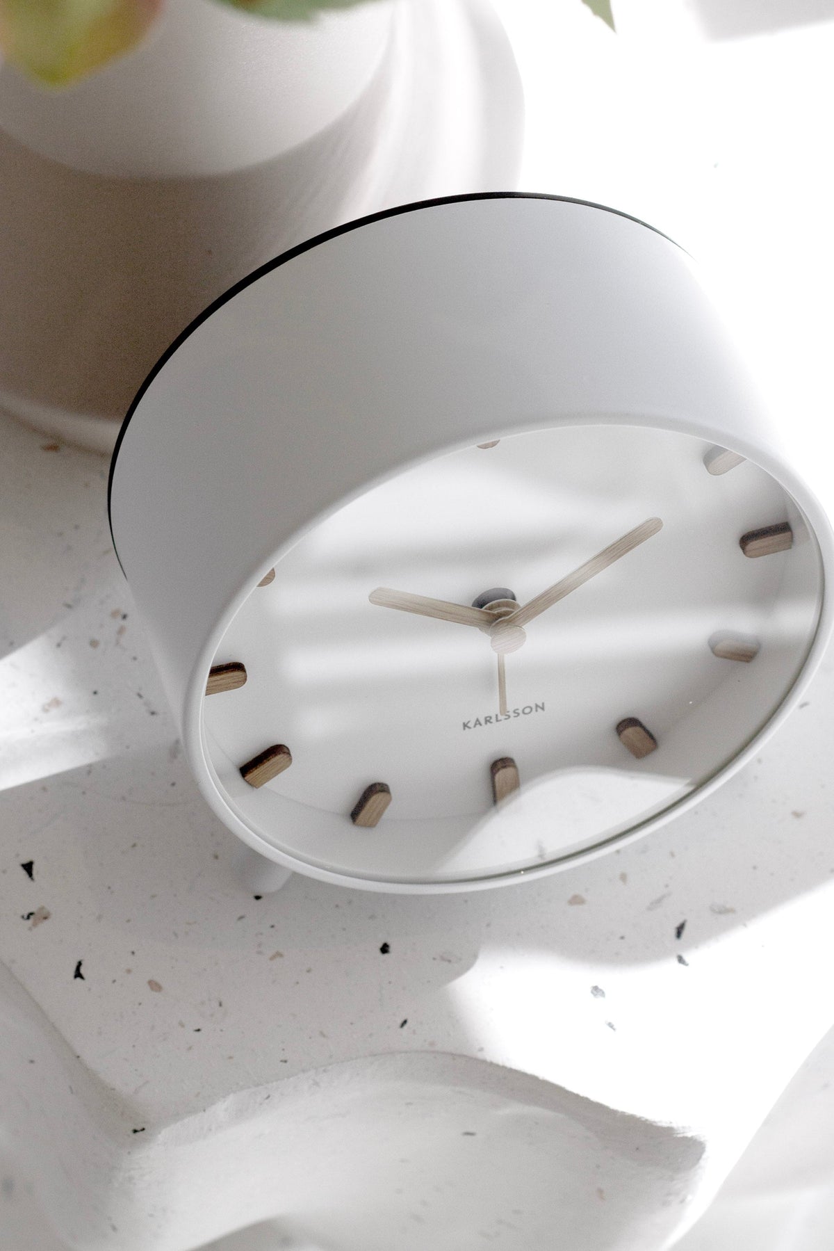 White Karlsson Grace alarm clock with wood-look markers styled on a soft white bedside surface.
