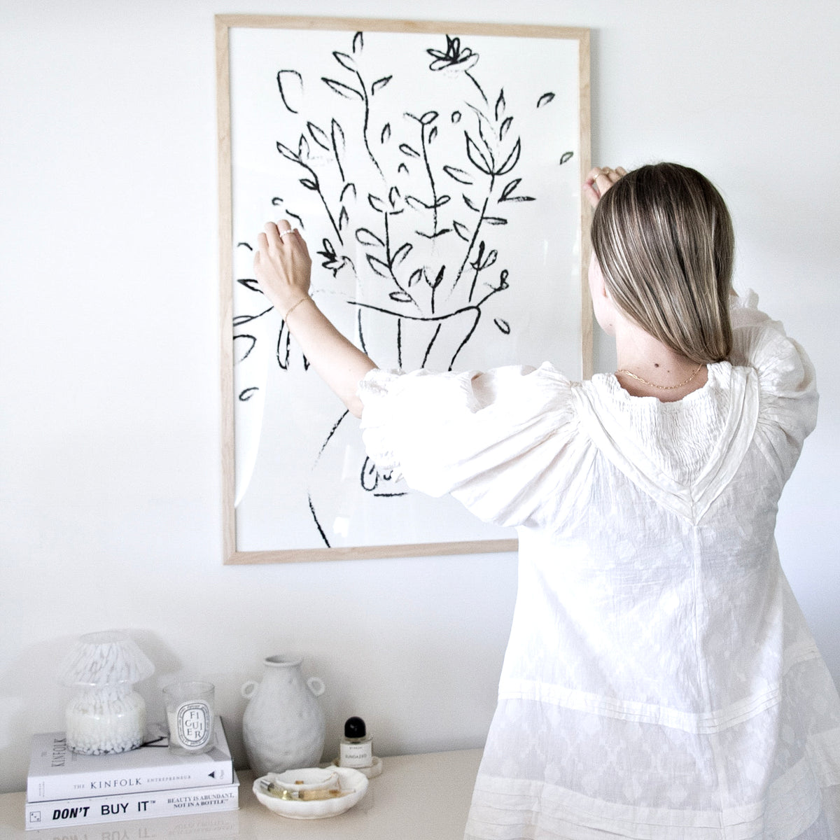 Woman hanging the Gucci Flowers print in a natural frame above a styled dresser