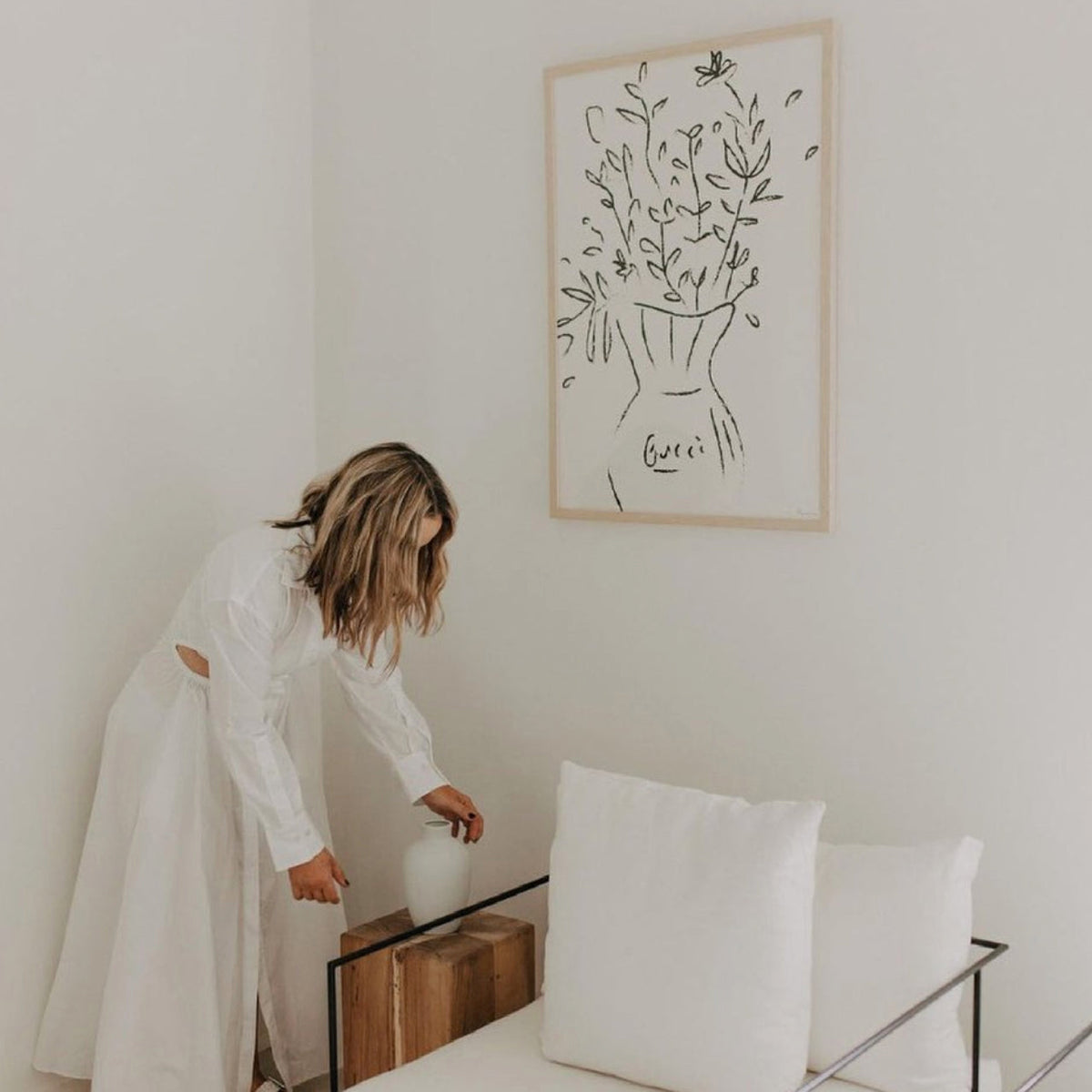 Woman styling a bedroom beneath the Gucci Flowers print in a natural frame