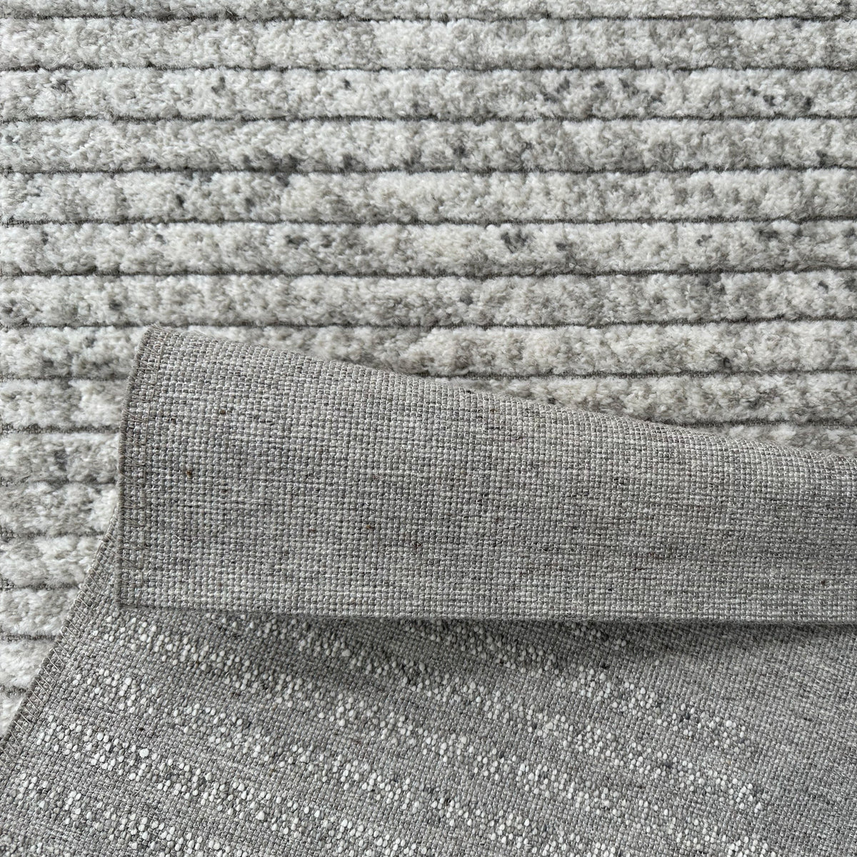 Folded edge showing the ridged grey and ivory pile and the woven backing