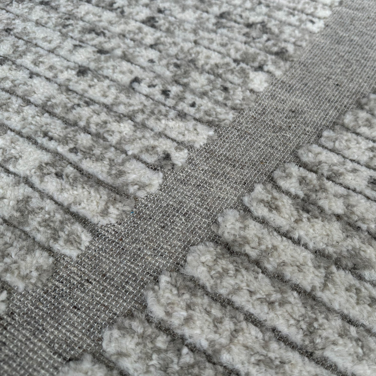 Close view of the raised ridged pile where an ivory curve meets the grey ground