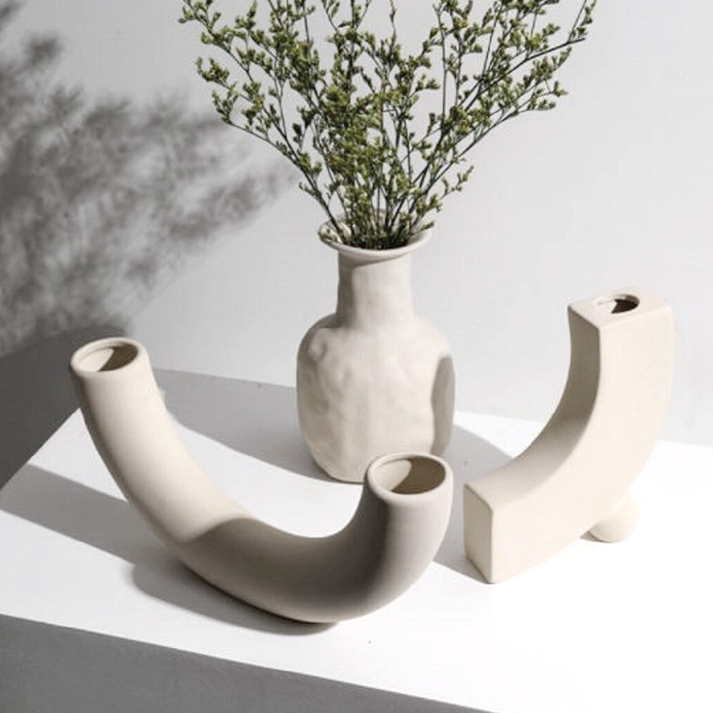 Half pipe vase with two other ceramics, one holding fine dried stems, on a white plinth