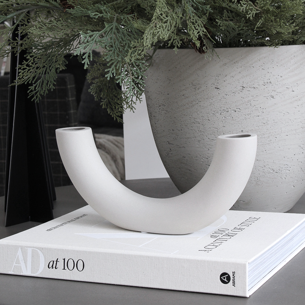 Half pipe vase set on a stack of design books with soft green foliage behind