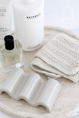 Handmade unbleached cotton face cloth on travertine tray with soap, skincare and lotion; eco-friendly washcloth.
