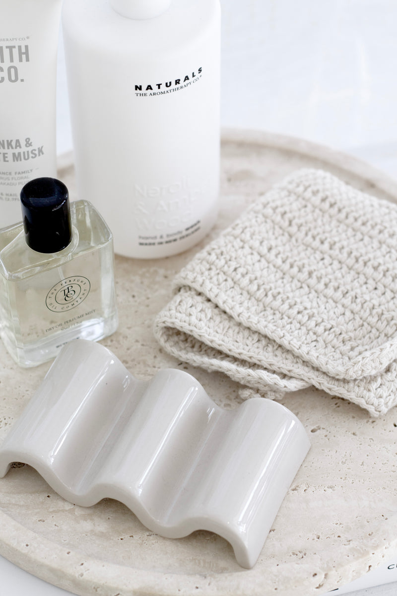 Handmade unbleached cotton face cloth on travertine tray with soap, skincare and lotion; eco-friendly washcloth.