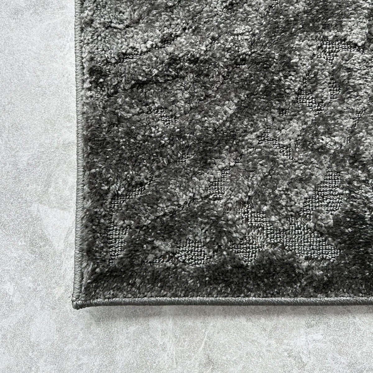 Corner of the dark grey indoor outdoor rug on pale stone