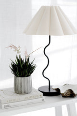 Faux Haworthia artificial plant in textured grey cement pot styled on stacked Kinfolk and Still coffee table books beside a wavy black table lamp with pleated white shade and oyster shell on a white side table