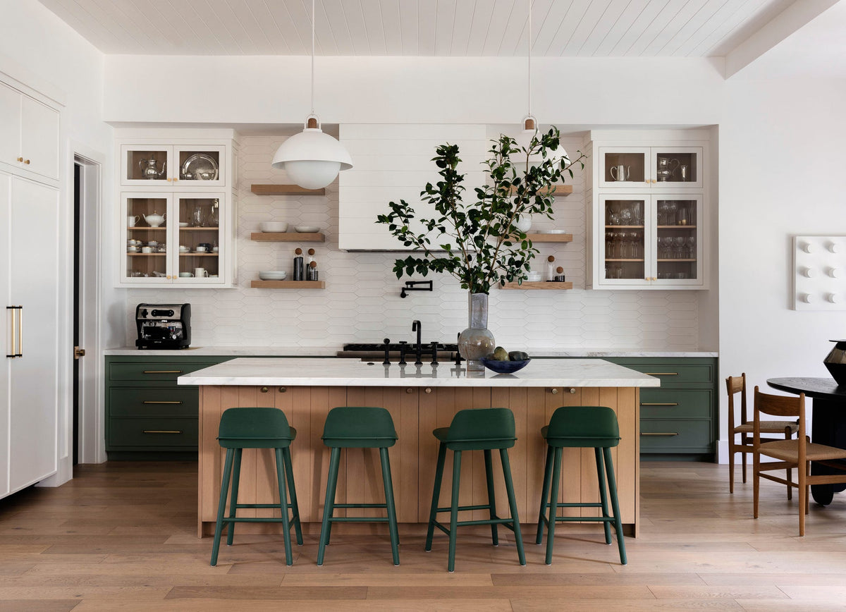 Interior from At Home: a white kitchen with a timber island and four green bar stools