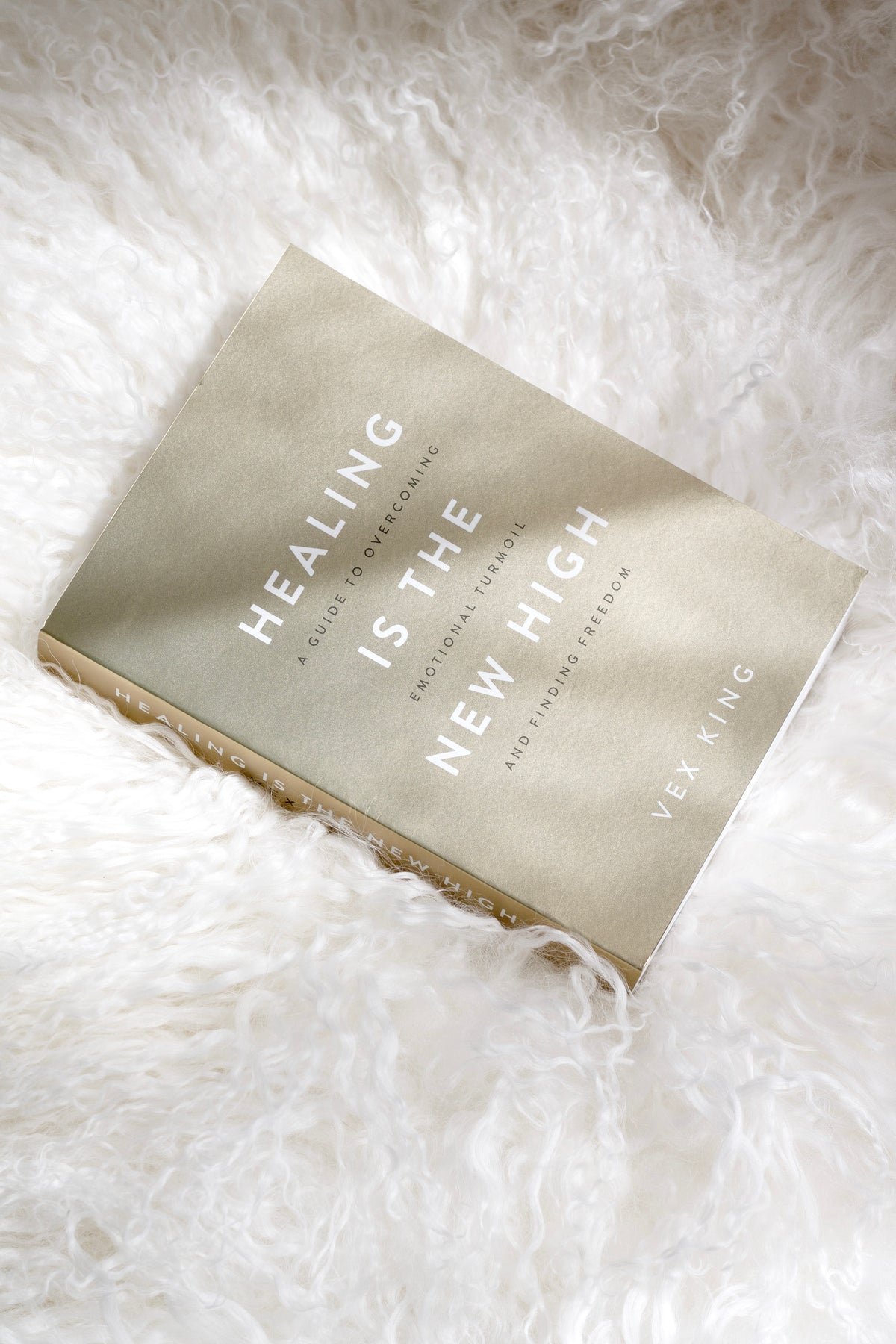 Healing Is The New High by Vex King book styled on white sheepskin throw