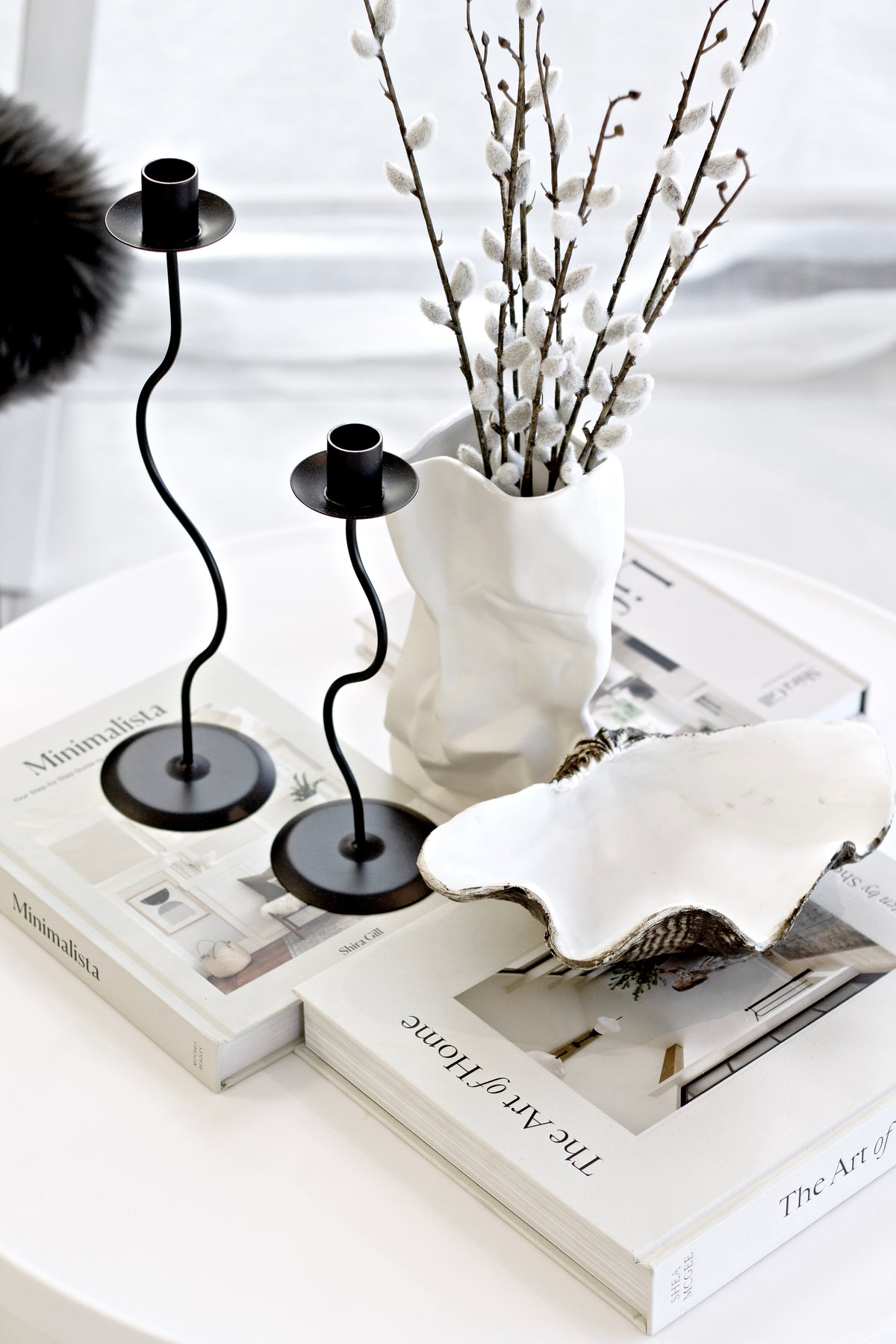 Overhead angle of the black Hera pair on books with a clam shell and pussy willow in a vase