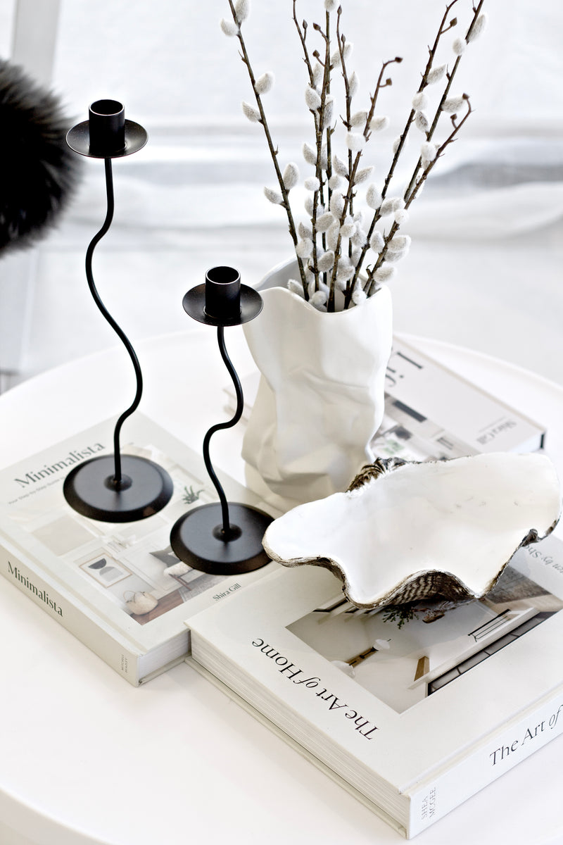 Pair of black sculptural curved candle holders styled with a ceramic vase and clam shell on coffee table books.