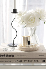 Home By The Sea book styled in a stack with Surf Shacks, a candle, marble dish, and white roses beside a sculptural black candleholder