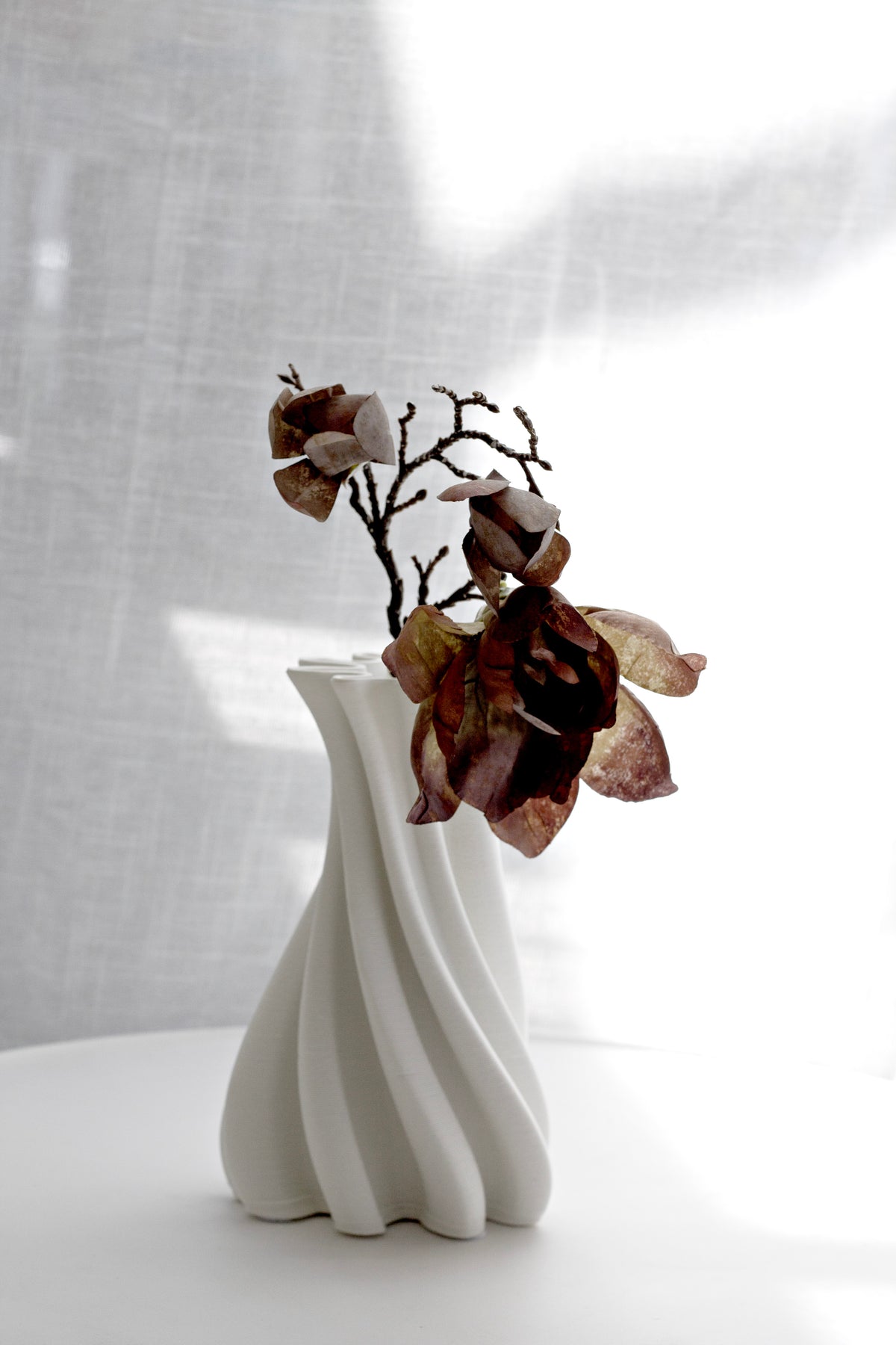 White Camila vase holding dried magnolia stems against a soft linen backdrop
