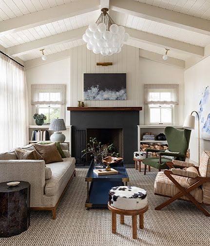 Interior from At Home: a living room with a black fireplace, vaulted white ceiling and a cowhide ottoman