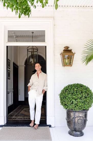 Man standing at a black front door beside a topiary in an urn