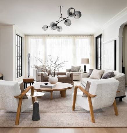 Interior from At Home: a white sitting room with sculptural timber armchairs and a branching pendant light