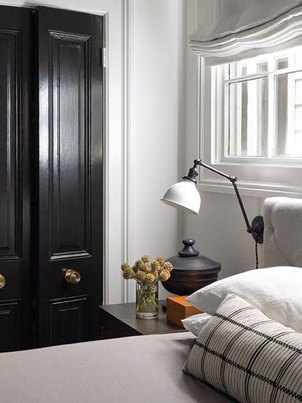 Interior from At Home: a glossy black door beside a bed with a wall lamp and a checked cushion