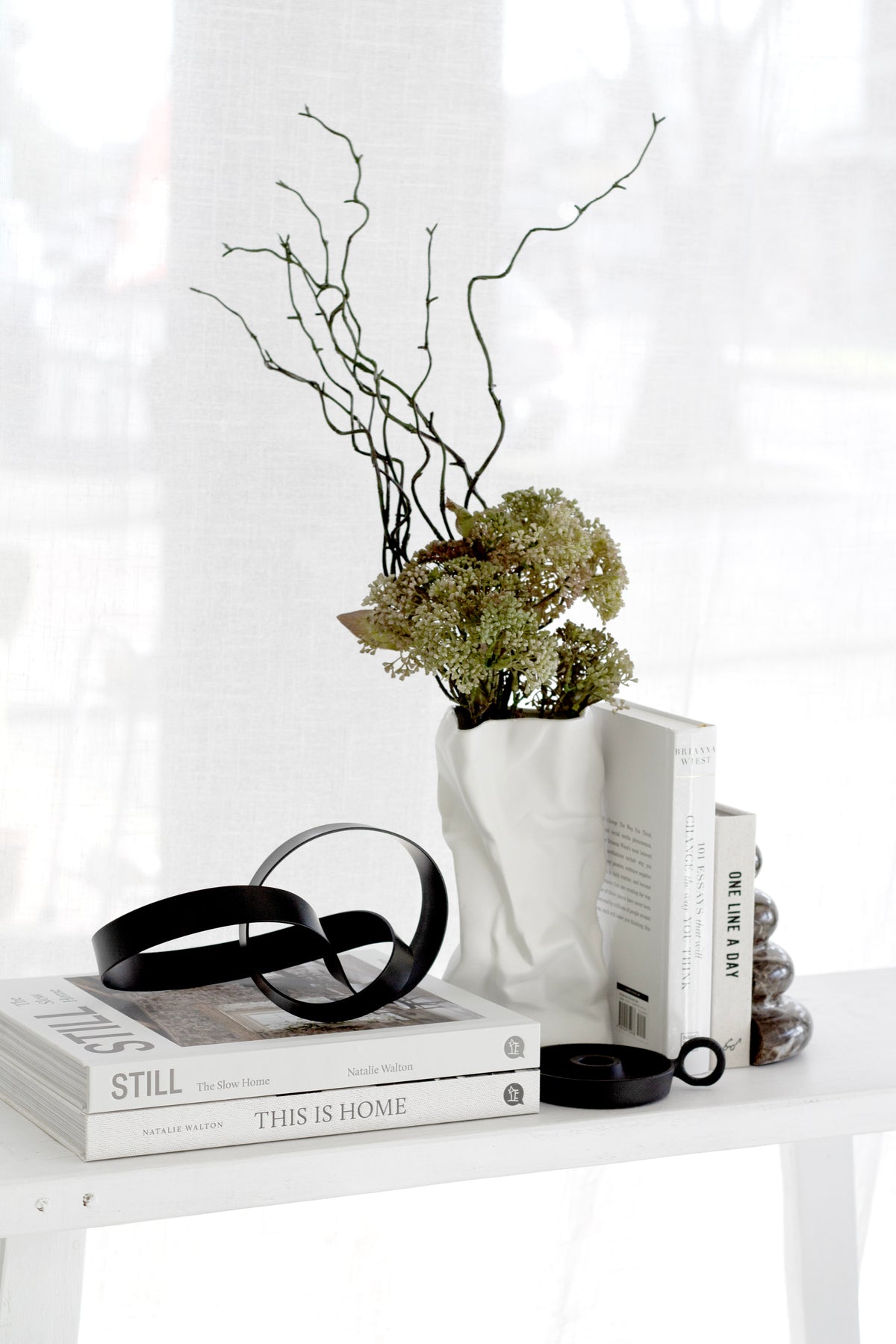Black Infinity Loop sculpture on stacked books beside a white vase of branches