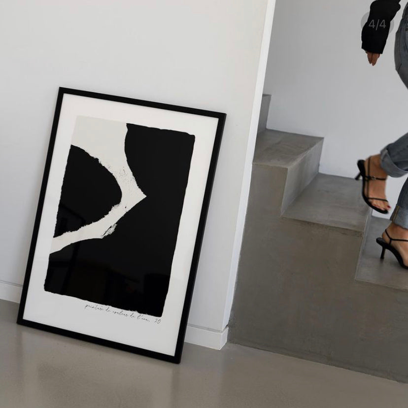 Ink print in black in a black frame leaning on the floor beside a staircase