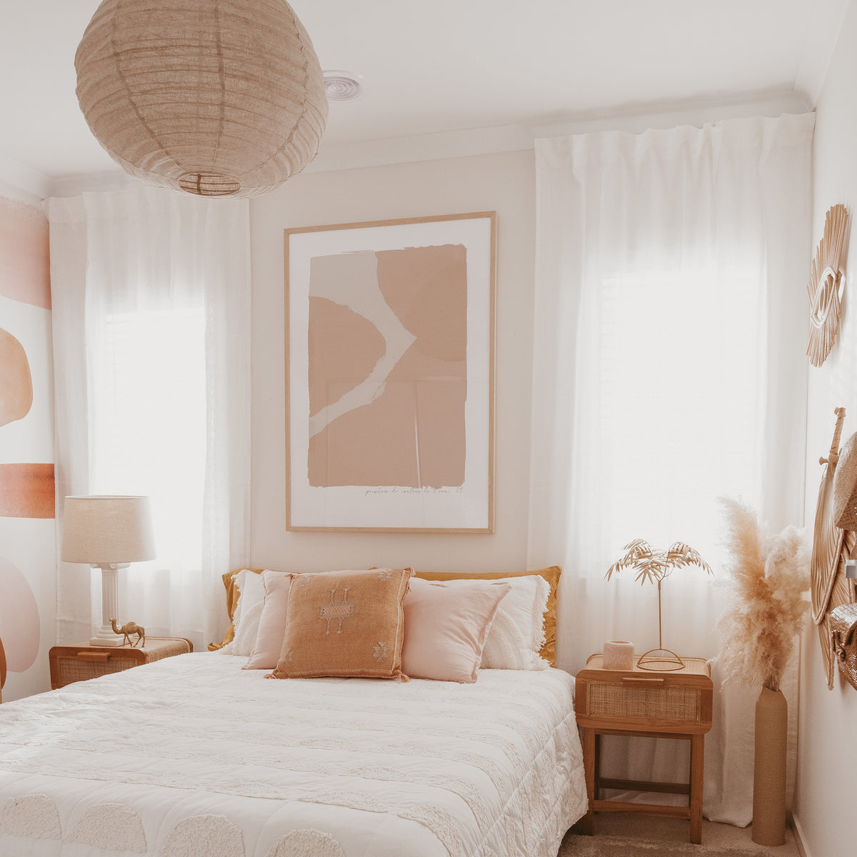 Ink print in pink in a natural frame above a bed in a soft neutral bedroom