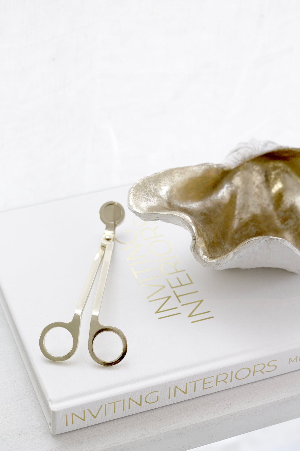Inviting Interiors book with gold candle snuffer and metallic decorative bowl styled on white surface