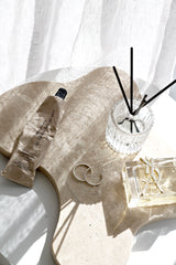 Travertine tray with hand cream, reed diffuser and jewellery styled in soft sunlight on white surface
