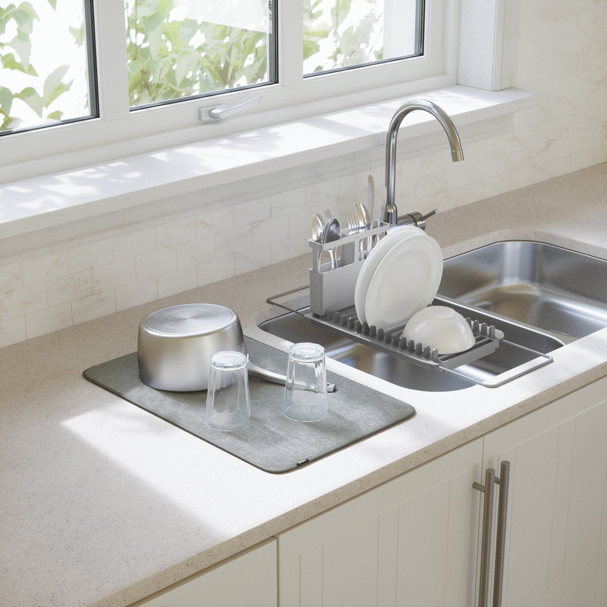 Umbra Udry dish rack over a kitchen sink with dishes drying on the mat below a window