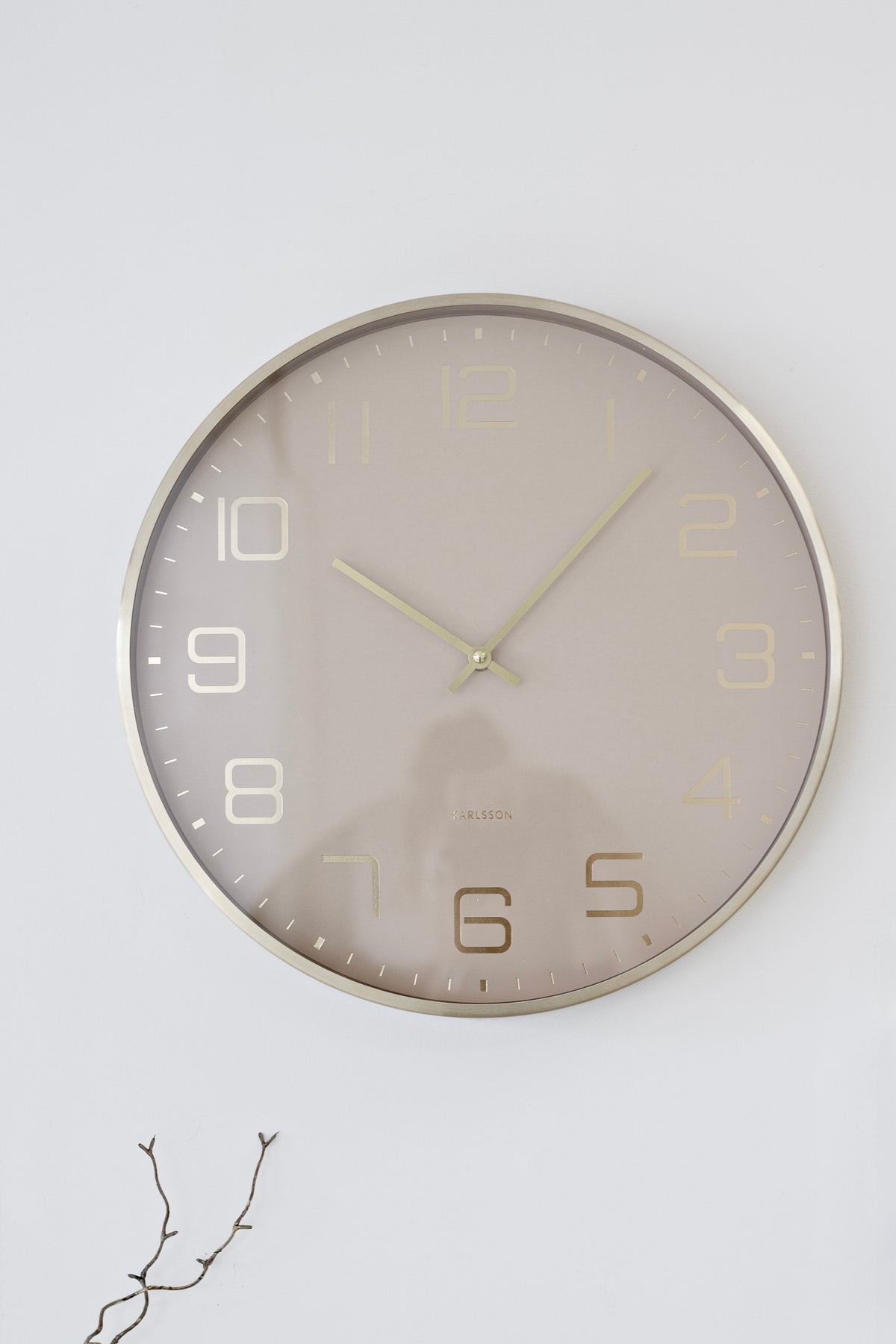 Karlsson Elegance Glow wall clock in soft brown with gold hands and a slim metallic rim on a white wall