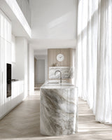 Karlsson Layered Lines wall clock in white on warm timber panel wall in minimal marble kitchen with floor-to-ceiling sheer curtains
