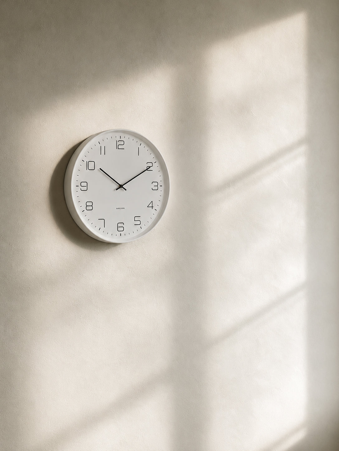 Karlsson Lofty Wall Clock matte white on textured plaster wall with warm afternoon window light and shadow