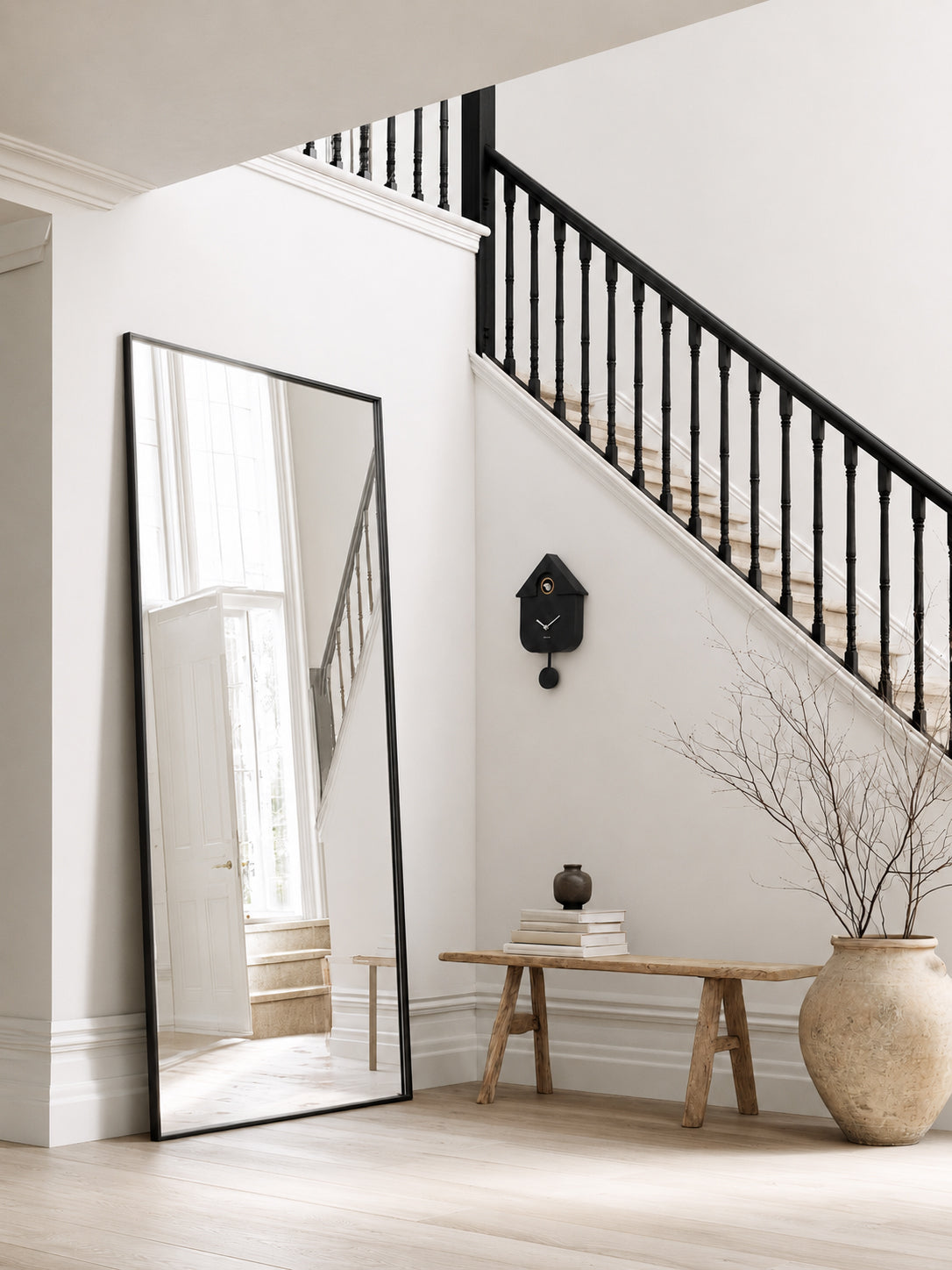Karlsson Modern Cuckoo Clock in black styled on hallway wall under staircase with leaning mirror and stoneware vase