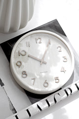 Karlsson pure wood grain wall clock in ivory styled on neutral surface with a coffee table book and vase