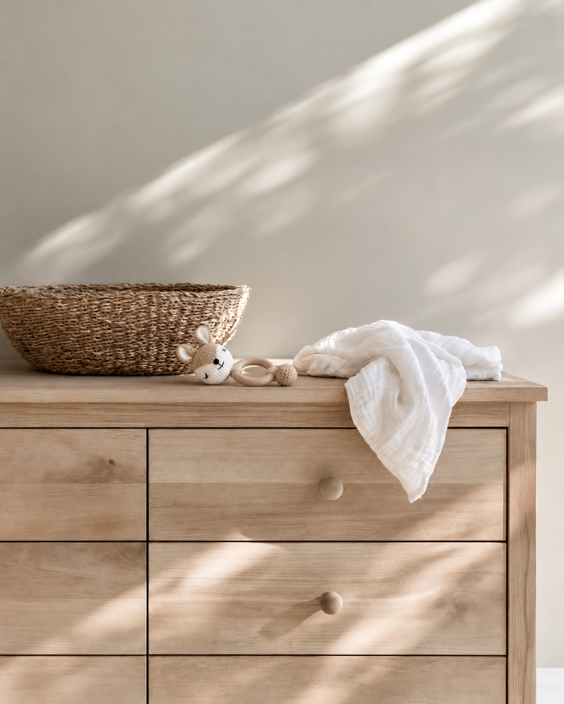 Miss Deer crochet wooden baby teether lying on an oak chest of drawers beside a woven basket and white muslin