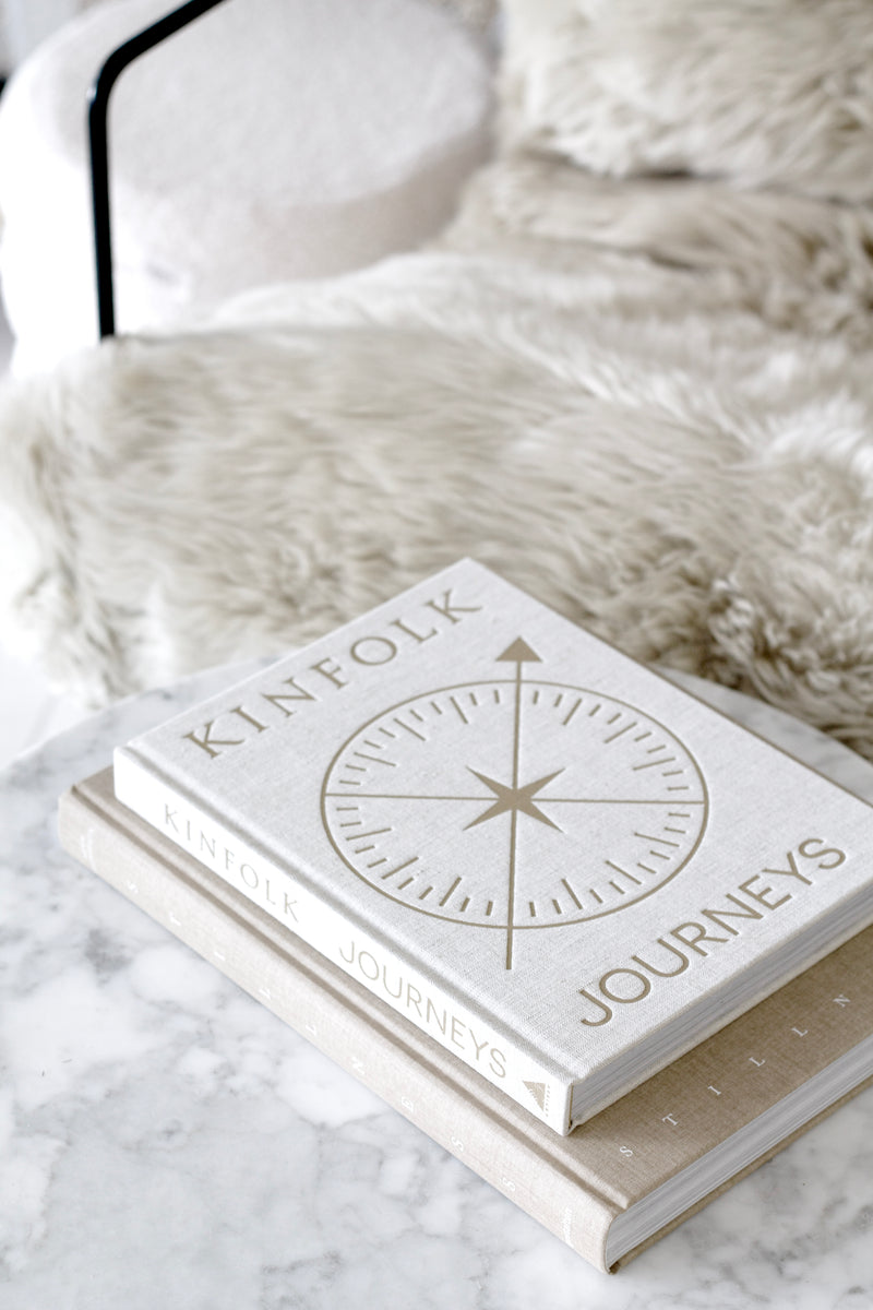 Kinfolk Journeys coffee table book styled on marble with neutral tones, showcasing its compass-inspired linen cover.