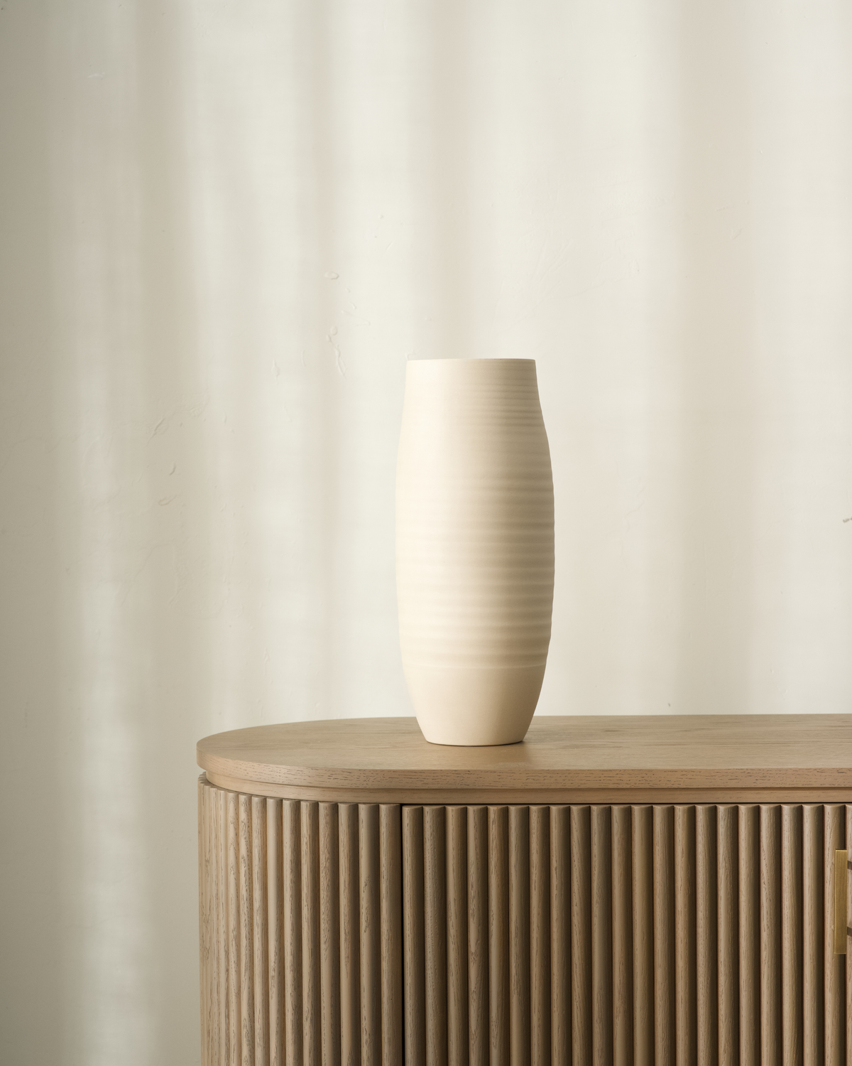 Large Beige vase in soft cream with fine wheel-thrown rings, standing on a fluted oak sideboard