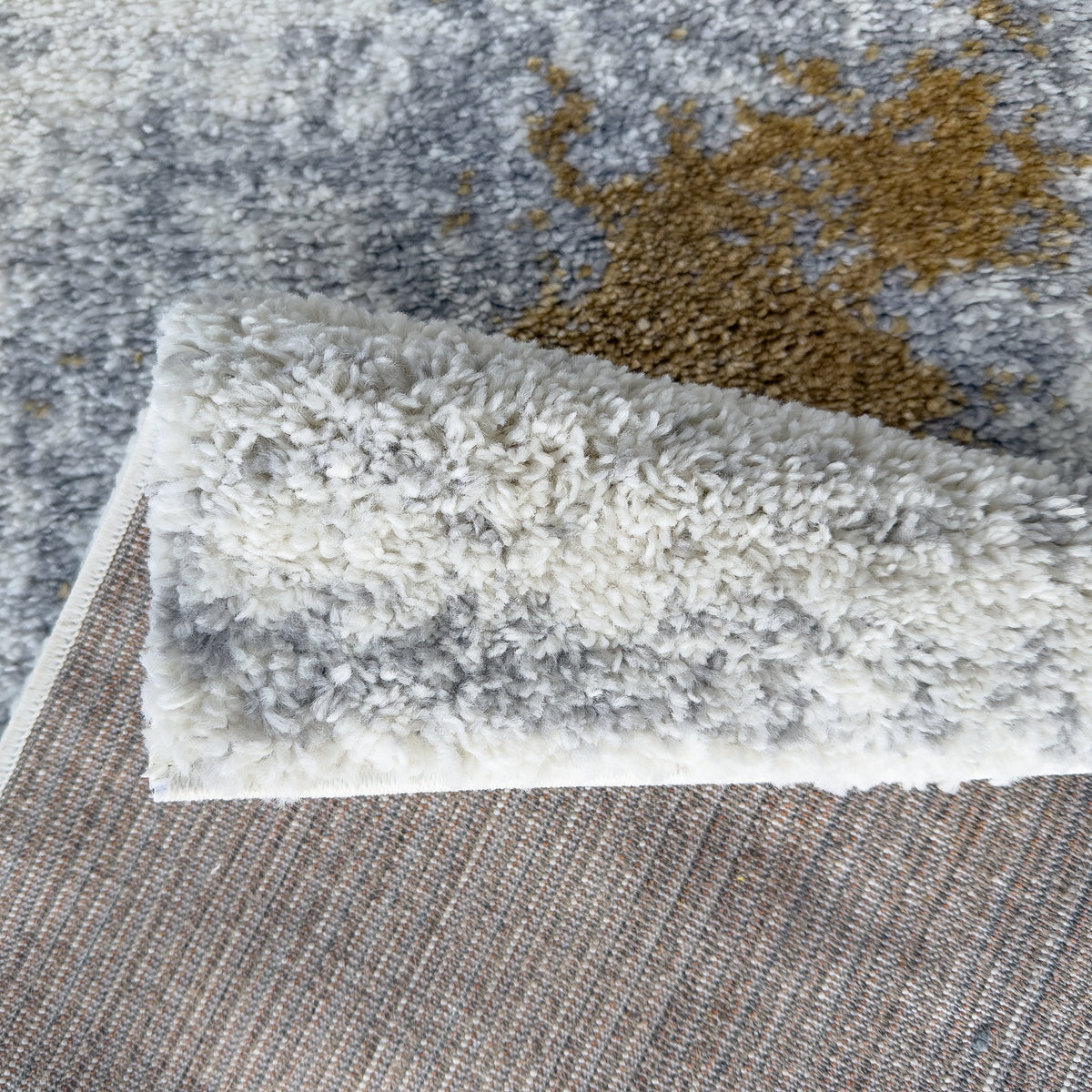 Grey and gold rug folded back to show the woven backing