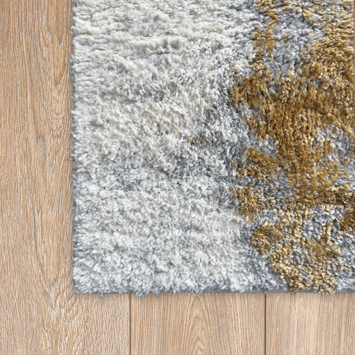 Corner of the grey and gold plush rug on a light timber floor