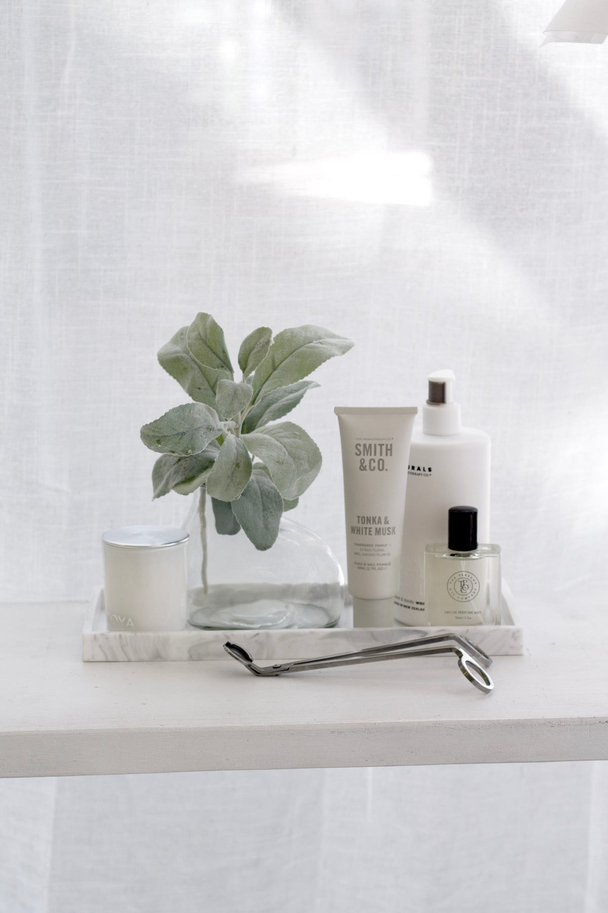 Velvety grey-green faux lamb’s ear stem styled in a clear vase on a marble tray with candles and lotions.