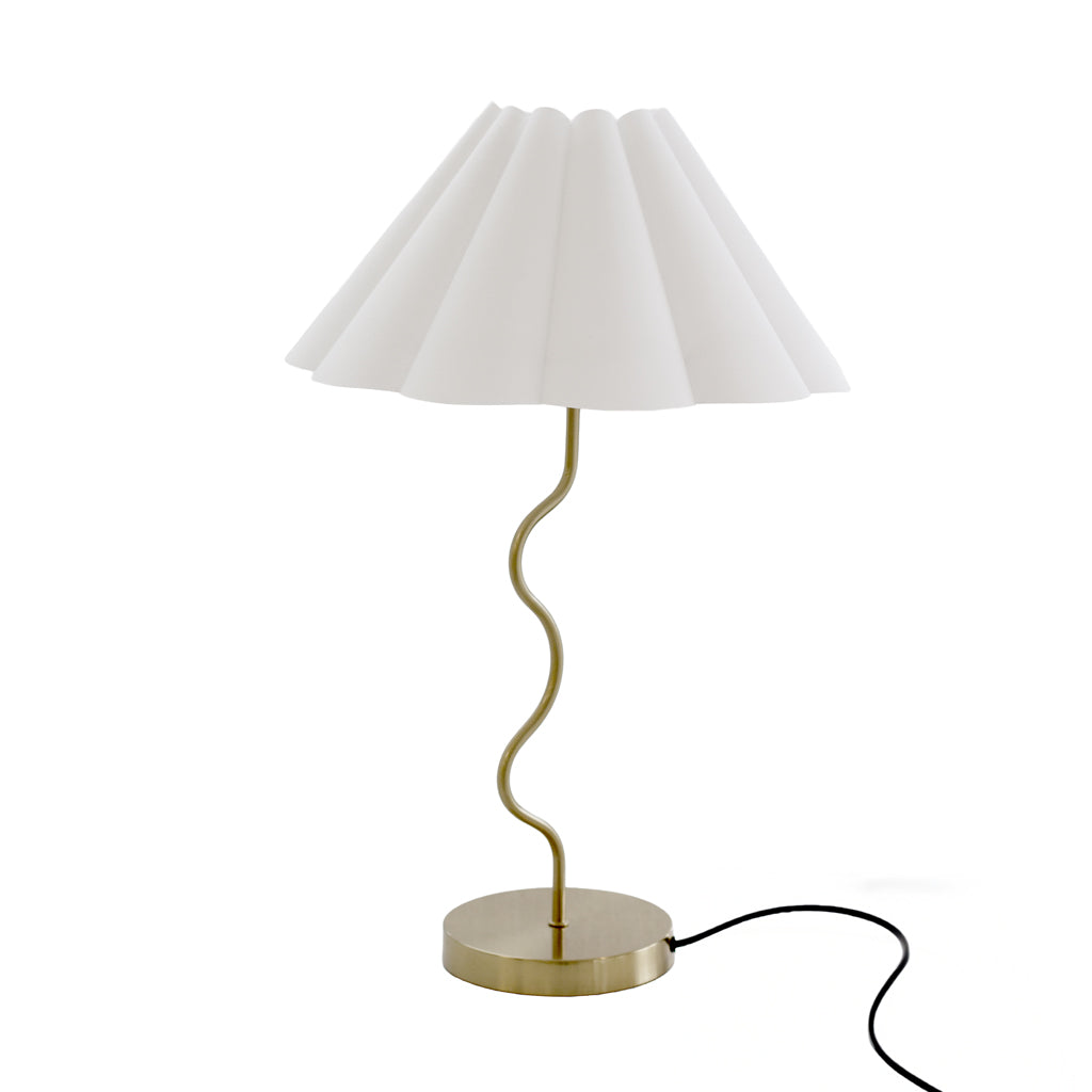 Wavy table lamp in brass with a pleated off-white fluted shade on a plain white background