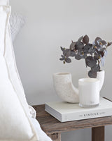 Brown eucalyptus spray faux stem styled in a speckled neutral vase beside an Ecoya candle on a bedside table with The Kinfolk Home book