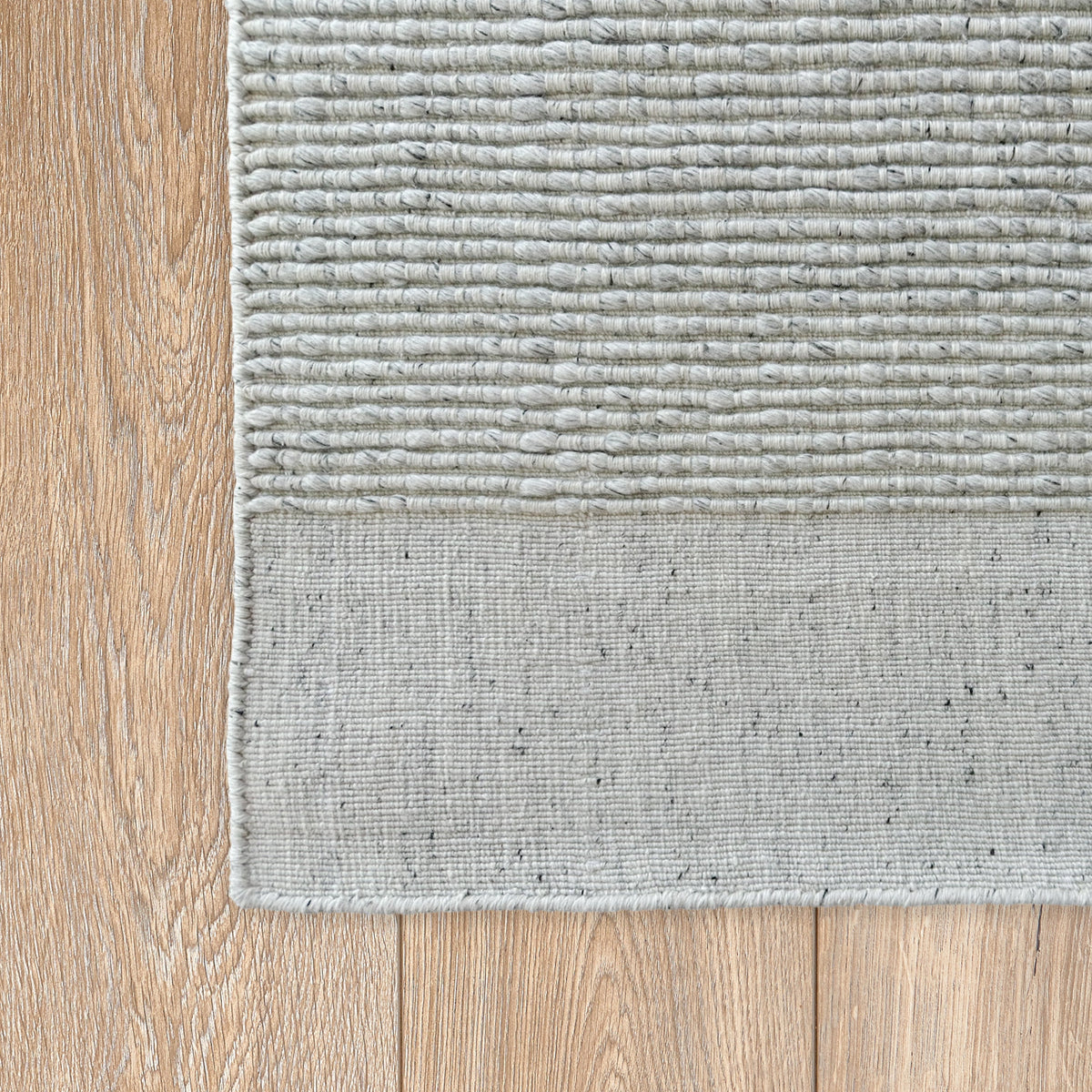Corner of the light grey rug showing the ribbed field and plain band on timber