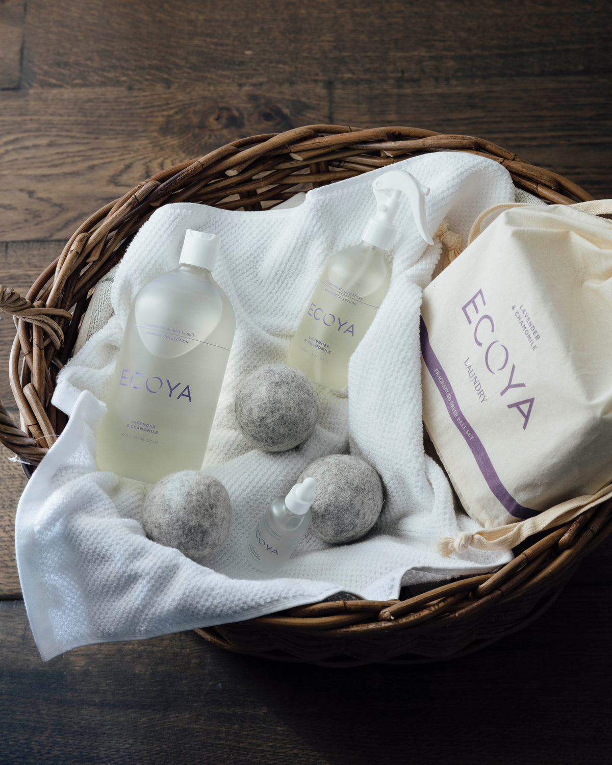 Wicker basket of white linen with Ecoya bottles, wool dryer balls and an Ecoya linen bag