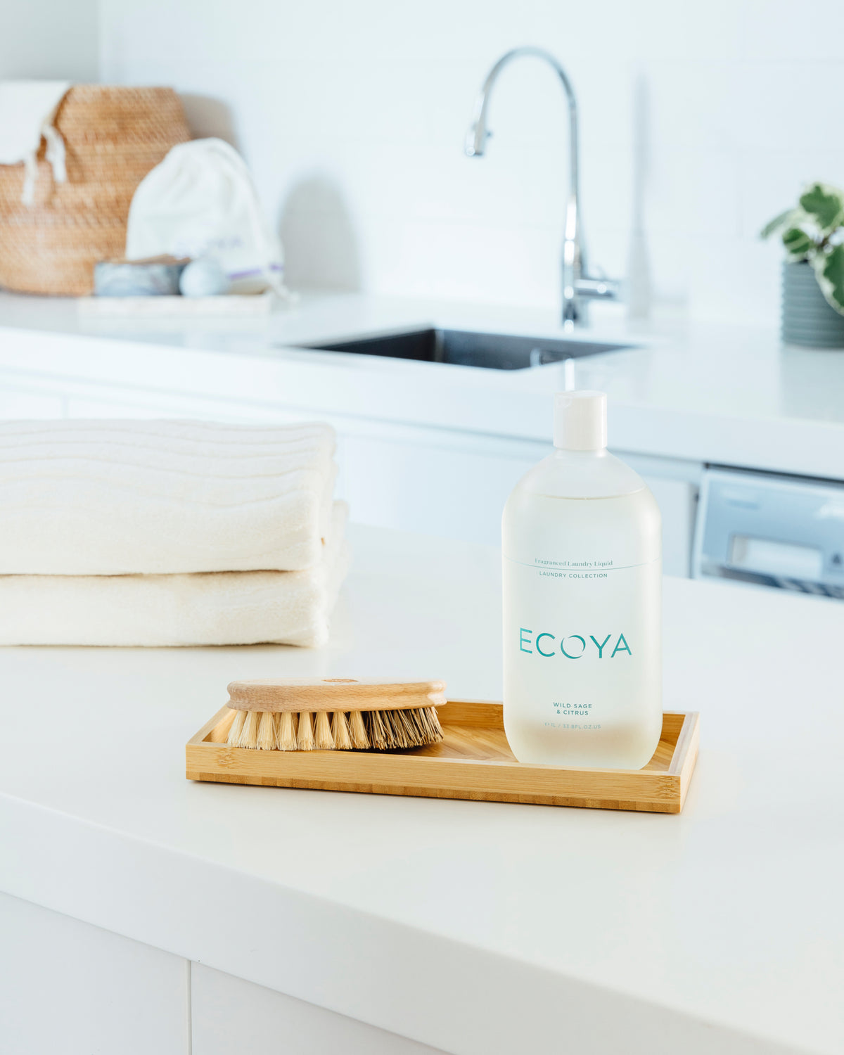 Ecoya Wild Sage and Citrus laundry liquid on a wooden tray with a brush beside folded towels