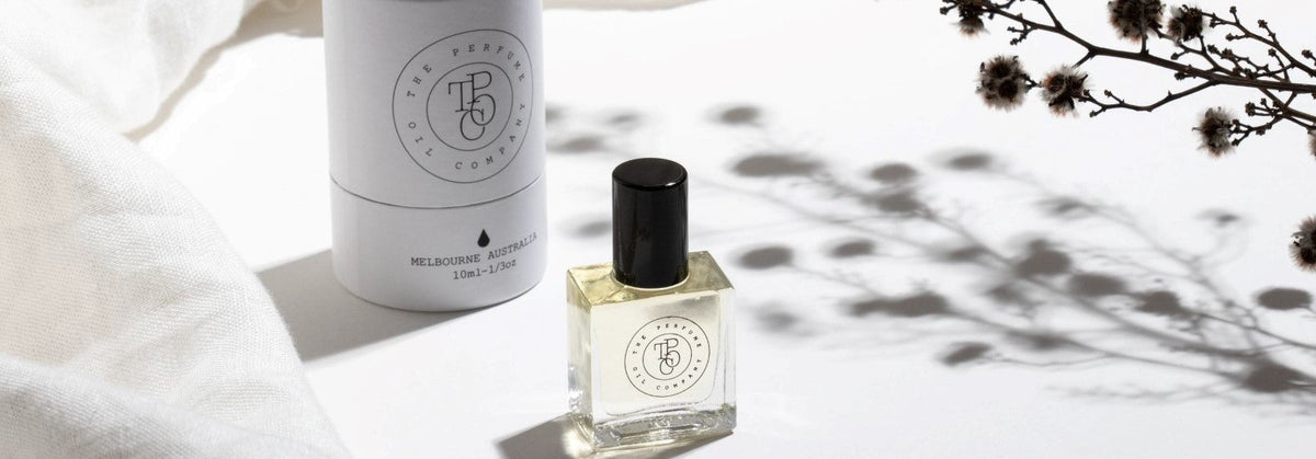 Roll-on perfume oil bottle beside a white tube carton on white linen with dried blossom