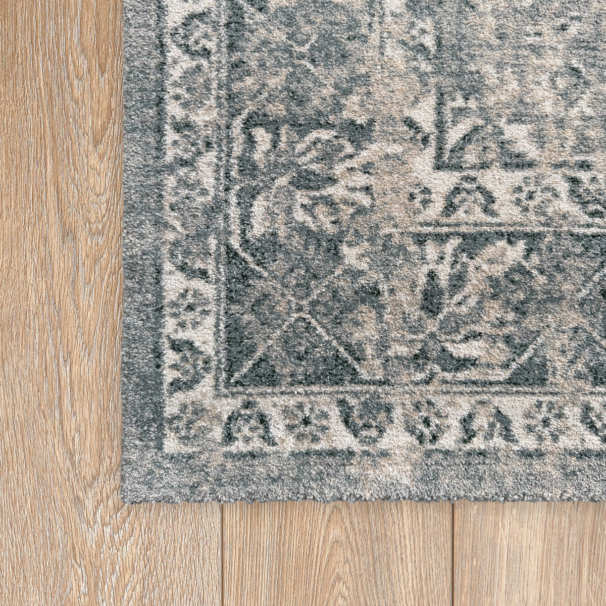 Corner of the stone grey rug showing layered borders on a timber floor