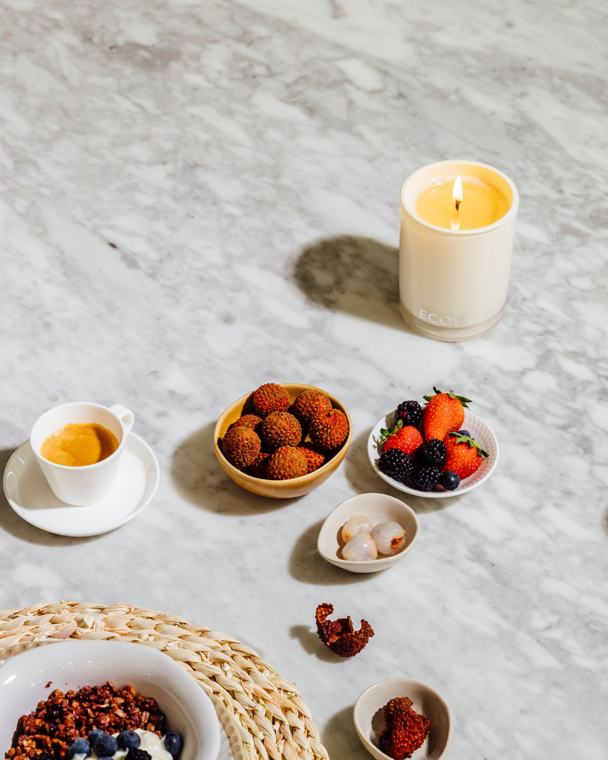Lit Ecoya Madison candle on a marble table with bowls of strawberries and cherries
